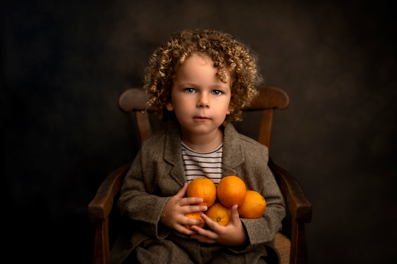 Petit garçon bouclé aux yeux bleus portant des oranges