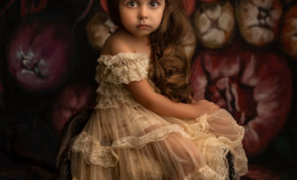 Petite fille au regard intense robe dentelle posant dans un décor fleuri