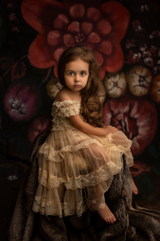Petite fille au regard intense robe dentelle posant dans un décor fleuri